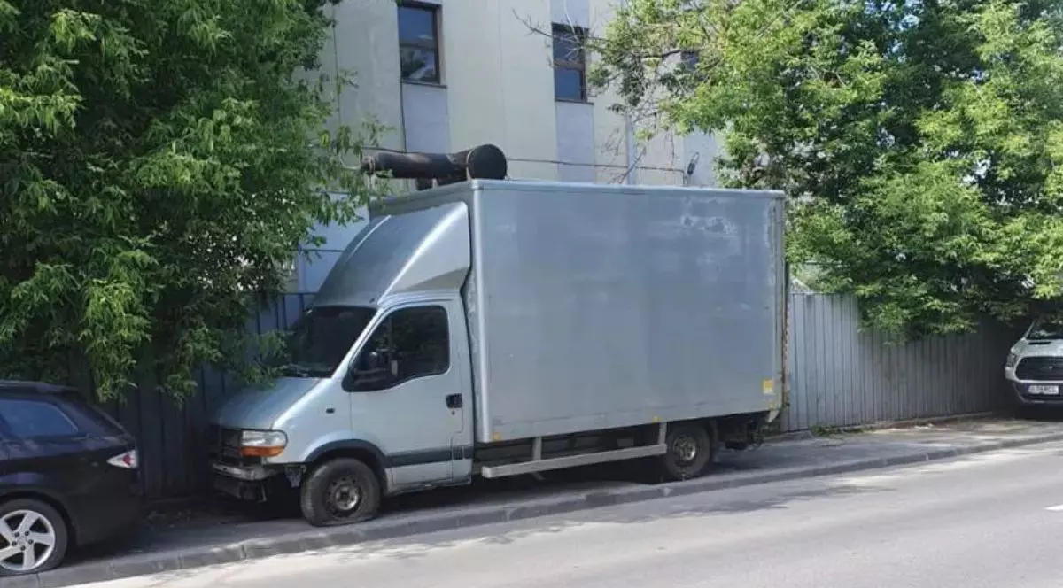 o duba parcata pe un trotuar in fata unui bloc de apartamente, copaci si stada goala