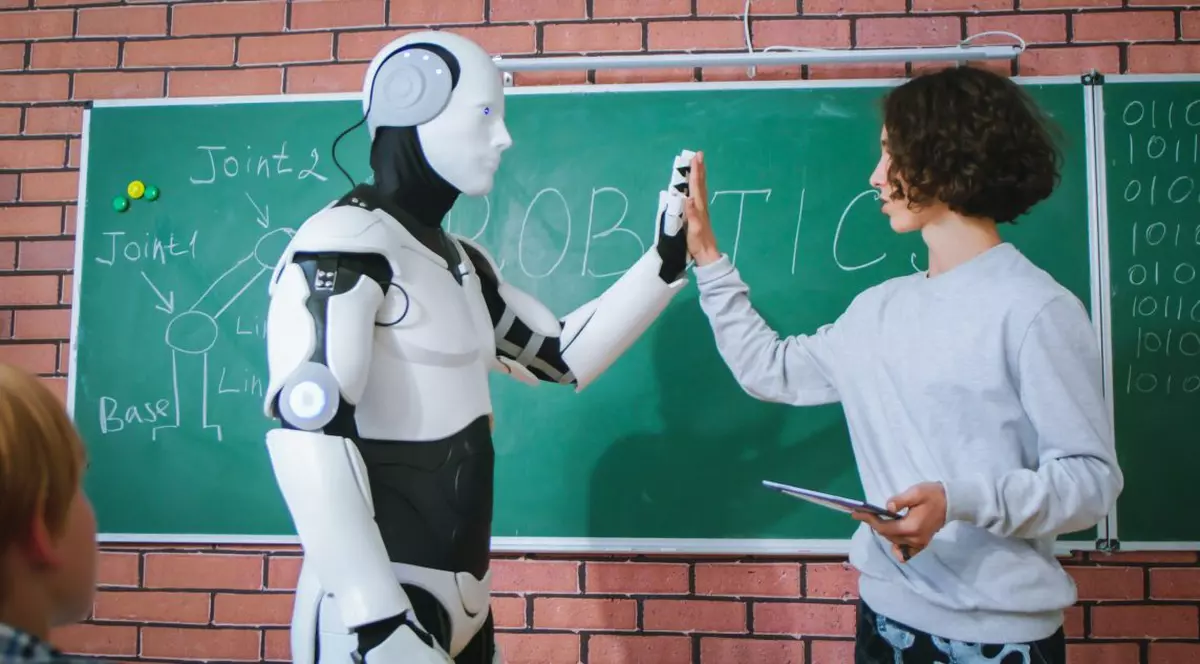 Elev în fața clasei la tabla alaturi de un robot umanoid