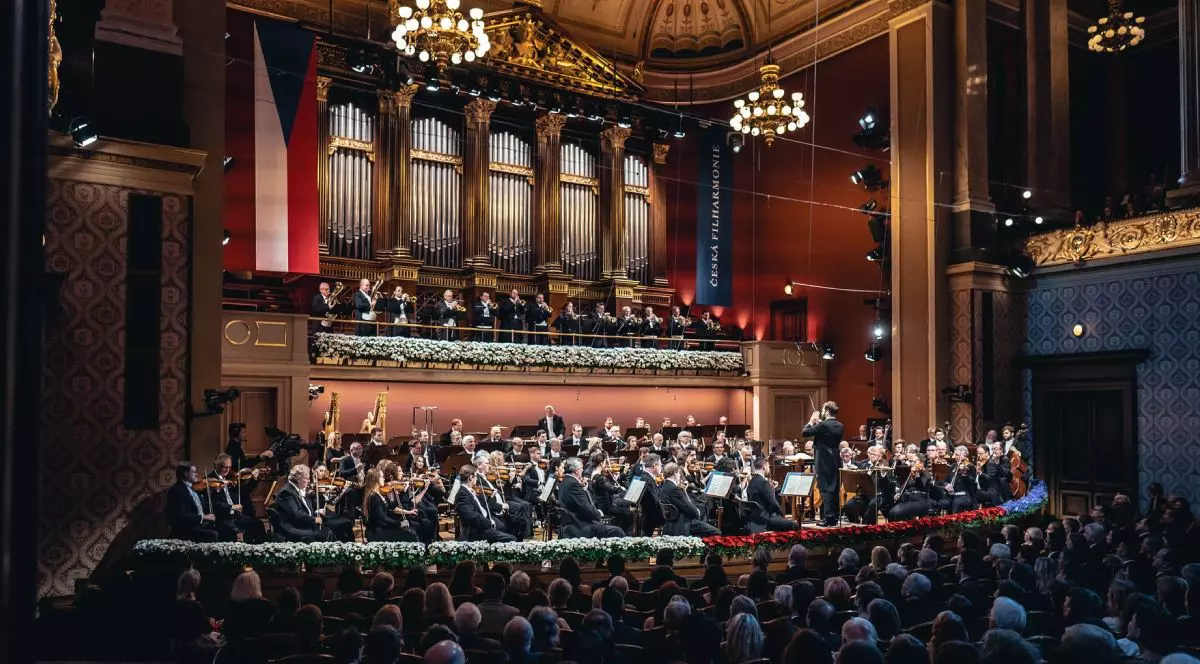 Mai mulți artiști cântă pe o scenă, în timpul Festivalului George Enescu 2025, in umnra se vede publicul, care sta pe scaune, se vad doua candelabre luminoase