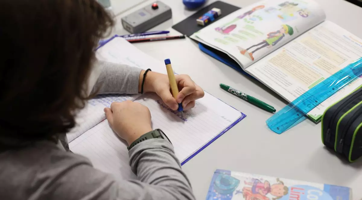 Un copil stă la masă și scrie ,având în față un manual de limba română, martie 2021