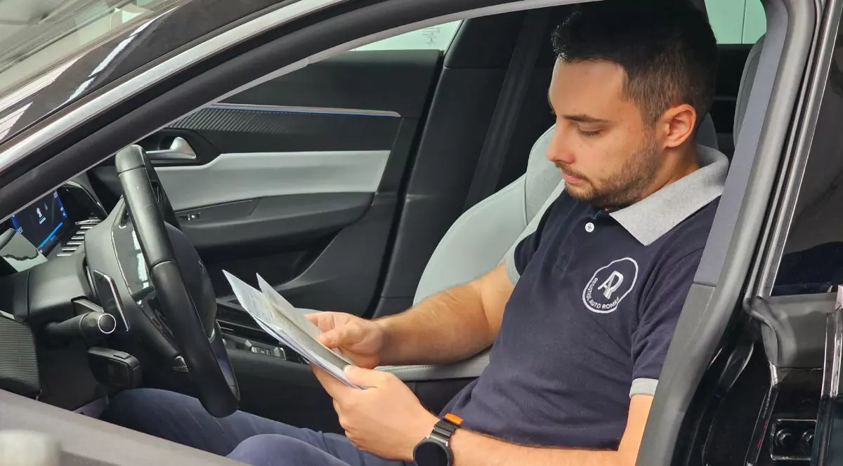 Un inginer RAR, îmbrăcat cu un tricou care are sigla RAR, în interiorul unei mașini, cu documente în mână