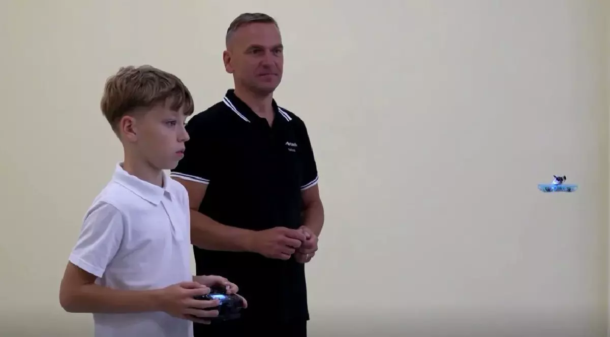 Un copil în tricou alb învață să piloteze o dronă, alături de un profesor în tricou negru, în Lituania, septembrie 2025