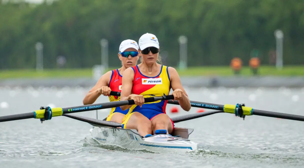 Magdalena Rusu și Simona Radiș în timpul unei probe de canotaj. Ambele canotoare poartă șepci și ochelari de soare, iar pe echipamentul lor se observă logo-ul Petrom
