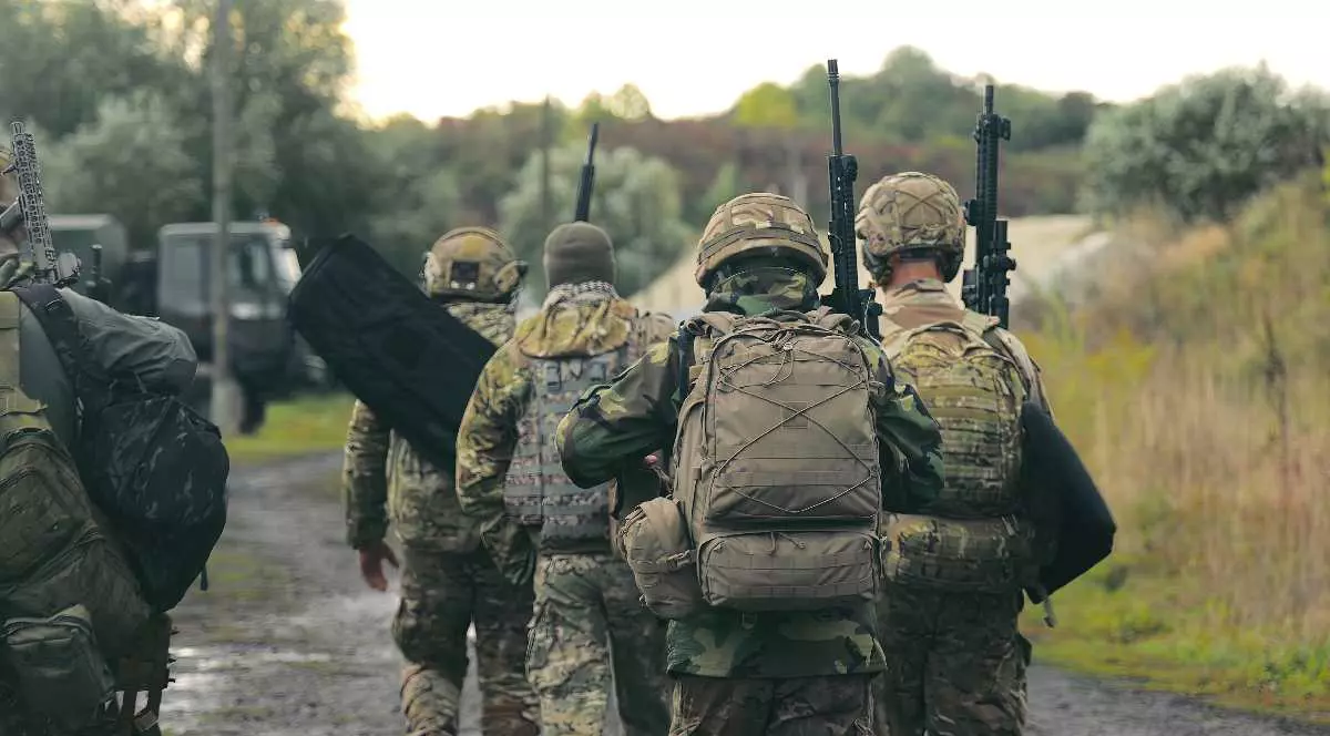 Soldați în uniformă militară cu mitraliere merg pe un drum pietros