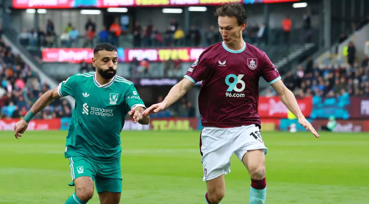 Mohamed Salah (stânga) îmbrăcat în echipament verde aleargă după minge și se contrează cu un adversar pe terenul de fotbal