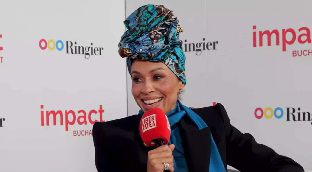 Omenaa Mensah ține microfonul LIbertatea în mână în timp ce vorbește despre afecrile sale și despre Impact București, pe cap are un turban extraordinar albastru cu turcoaz