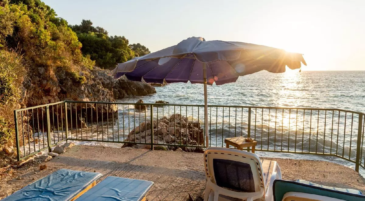 Utjeha, Muntenegru, 22 august 2025, Plajă cu pietriș amenajată pe malul Mării Adriatice, șezlonguri și umbrele goale la apusul soarelui, Utjeha, Muntenegru