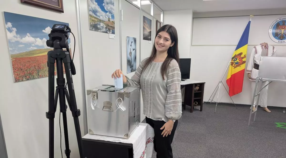 o tânără brunetă, îmbrăcată în pantaloni negri și un pulover gri cu mâneci evazate introduce un vot într-o urnă transparentă, la Ambasada Republicii Moldova în Tokyo, 28 septembrie 2025