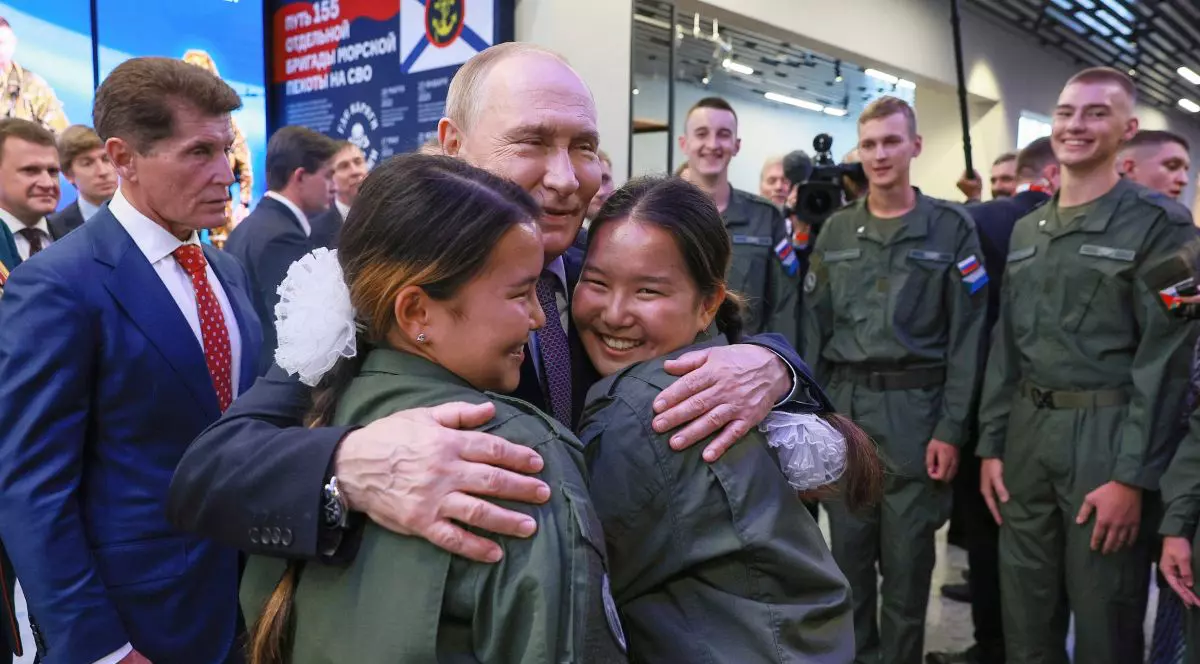 Vladimir Putin îmbrățișează râzînd două tinere îmbrăcate în uniformă militară