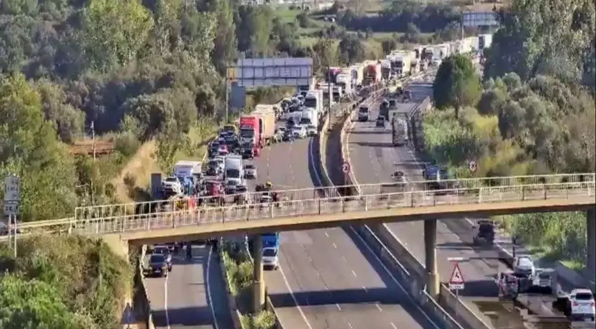 În prim-plan se vede o pasarelă, iar jos o autostradă cu mai multe sensuri de mers unde a avut loc un accident între două TIR-uri și s-a format o coloană de mașini în spate, în Spania, 19 septembrie 2025.