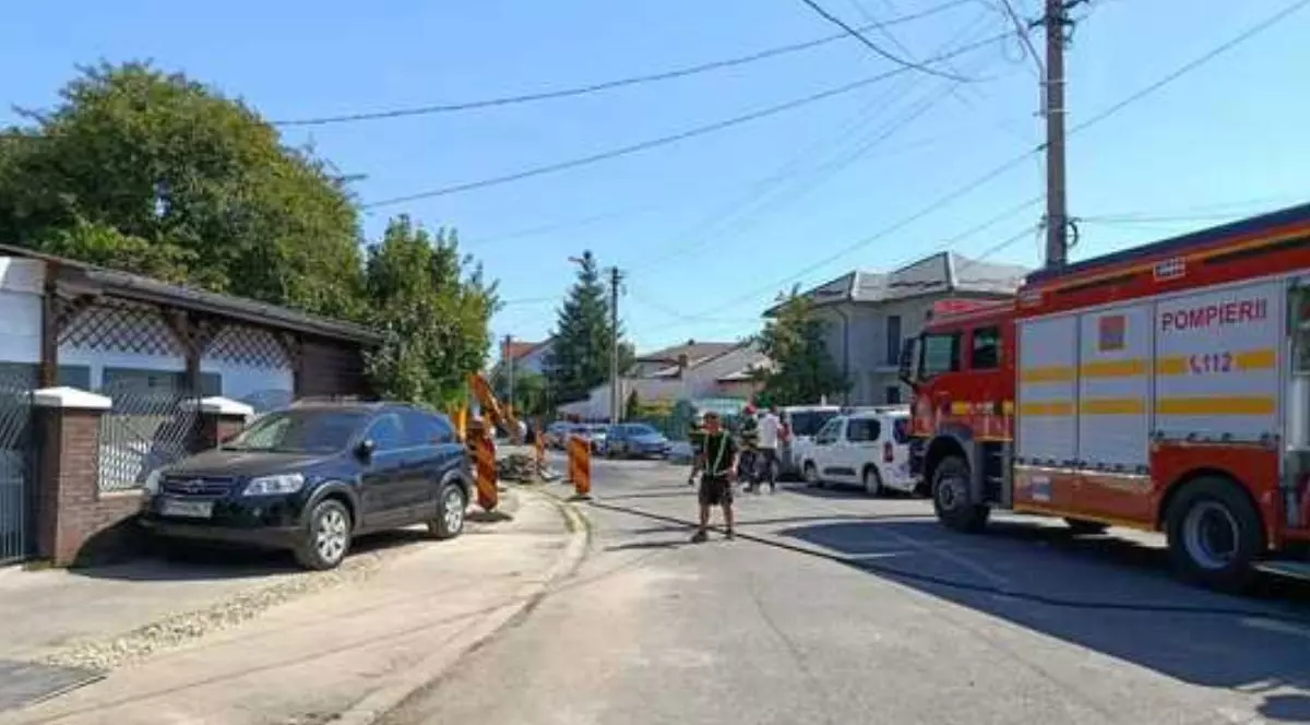 În imagine o masina de pompieri in stanga, pe strada plina cu masini se vad mai multi salvatori si o zona unde se lucreaza, semnalizata prin stalpi rosu - galbeni, copaci verzi