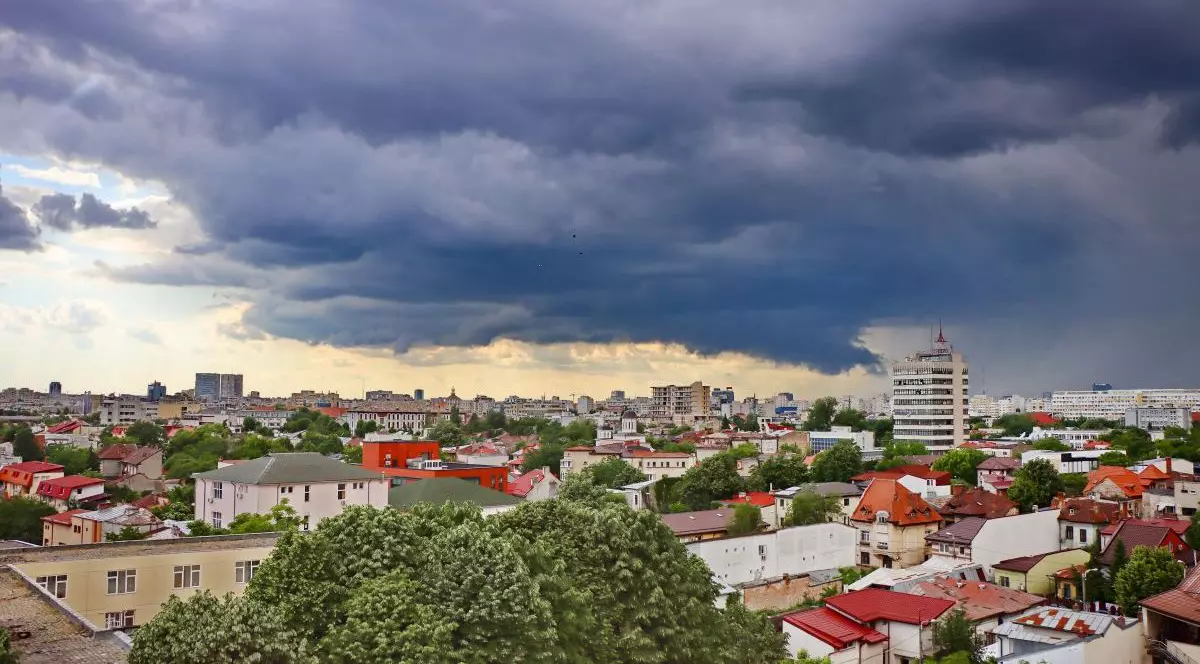 Nori de furtună și ploaie deasupra orașului, vedere de sus, iar în partea de jos se văd blocuri, case și pomi, în București