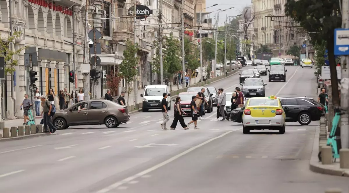 Mai mulți oameni sunt pe trecere și traversează strada, pe bulevard sunt mașini oprite la semafor în ambele sensuri, iar în jur se văd clădiri și copaci, București, 16 septembrie 2025