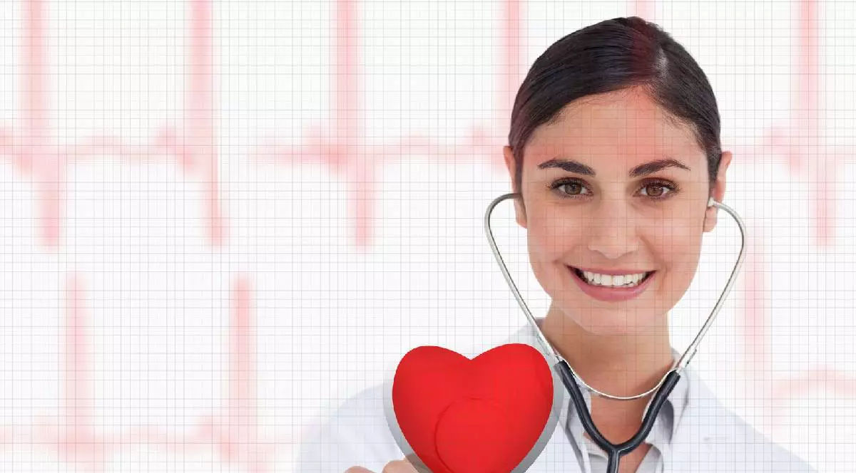 O doamnă doctor ține în mână o inimă roșie și zâmbește, în urechi are brațele unui stetoscop și e îmbrăcată cu un halat alb