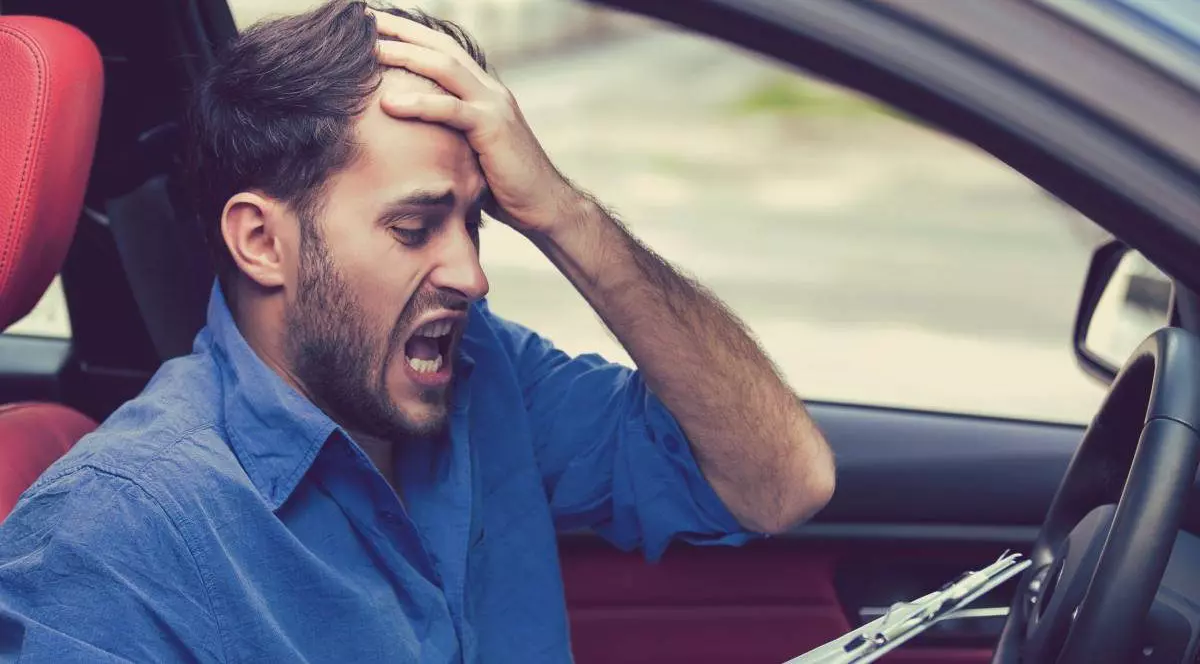 Tânăr şofer disperat, cu mana stanga la cap, tipand, cu hârtii - amenzi in mana dreapta, stând în interiorul maşinii sale