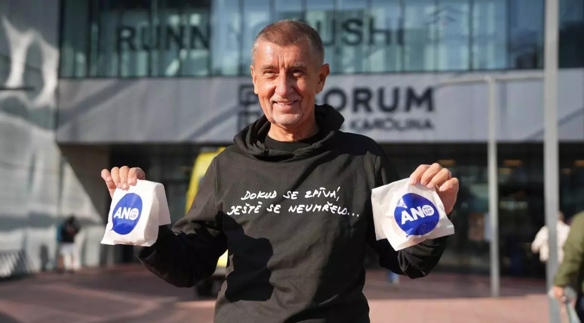 Miliardarul Andrei Babis. cu un hanorac negru cu un scris alb, cu mainile ridicate si cate o punguta alba cu inscriptie albastra in fiecare mana, a împărțit gogoși în prima zi de vot din Cehia, octombrie 2025