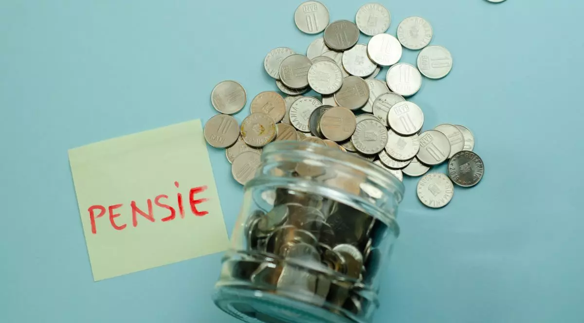 Un borcan de sticlă răsturnat, cu monede care sunt împrăștiate, lângă un postit cu textul pensie, pe fundal albastru deschis