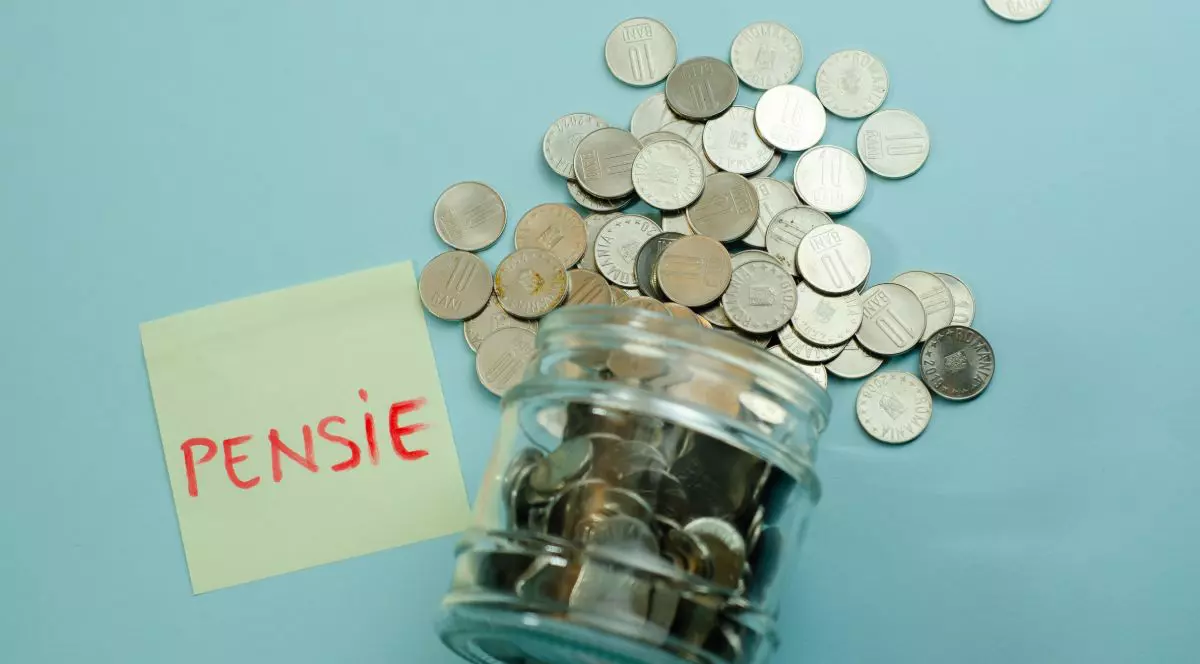 Un borcan de sticlă răsturnat, cu monede care sunt împrăștiate, lângă un postit cu textul pensie, pe fundal albastru deschis