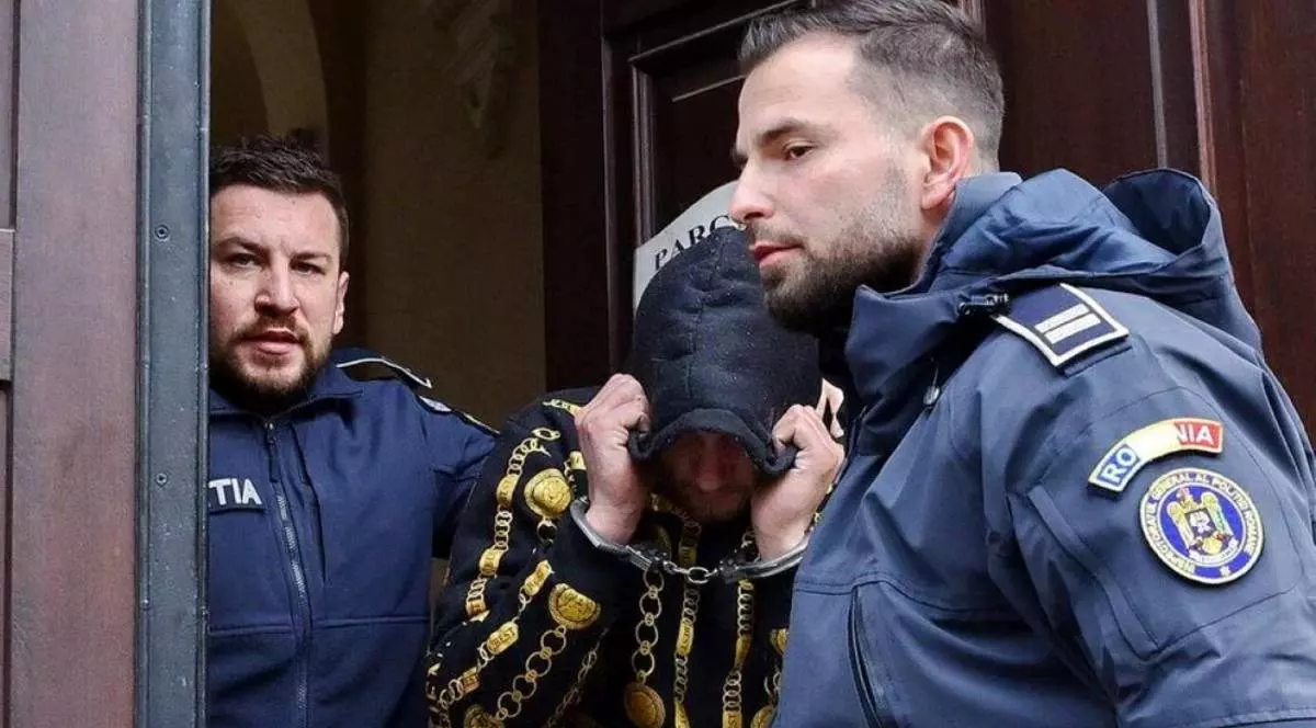 Un barbat încătusat, cu mainile legate ridicate la cap, langa el doi politisti