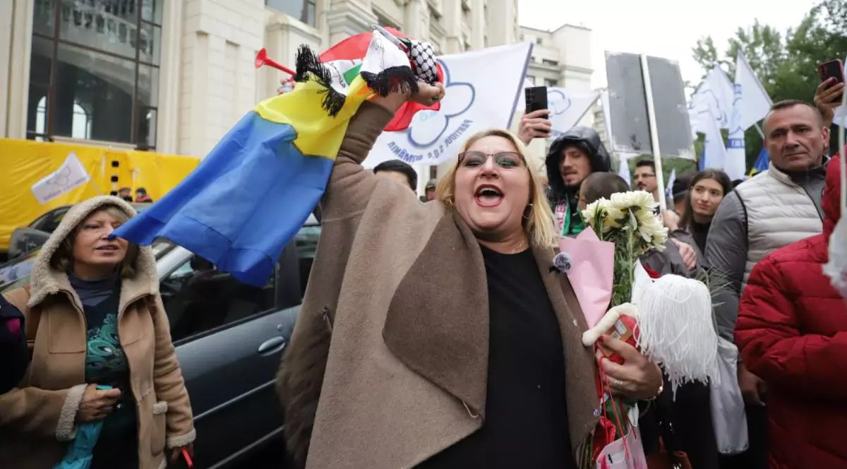 Diana Șoșoacă la Parchetul General, inconjurata de o multiime de oameni, in haina maro deschis si bluza neagra, cu mana dreapta ridicata , tinand steagul României, mana stanga stransa la piept, tinand flori albe, o papusa si o punga de cadouri roz. 6 octombrie 2025 Foto Dumitru Angelescu