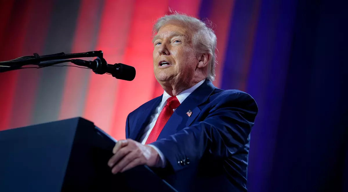 Imaginea îl prezintă pe Donald Trump vorbind la un pupitru în cadrul unui eveniment, îmbrăcat într-un costum bleumarin și o cravată roșie. Fundalul este iluminat dramatic în culorile roșu și albastru, sugerând o scenă politică sau de campanie.