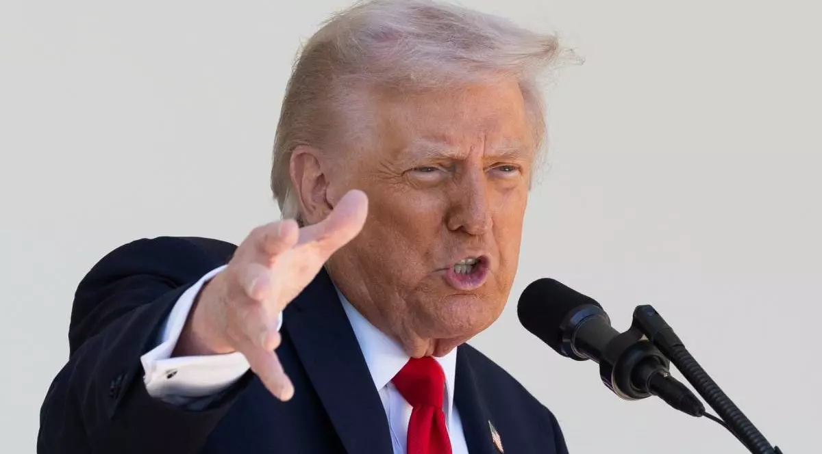 Donald Trump, președintele SUA, in sacou negru, camasă albă si cravata, rosie, cu mana dreapta ridicata si palma deschisa, orientata in fata, surprins in timp ce vorbeste la microfon