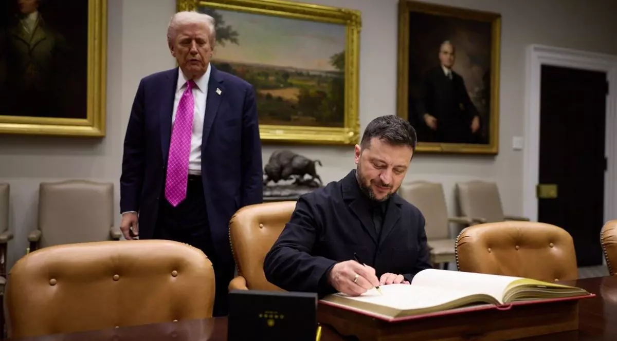 Președintele Ucrainei, Volodimir Zelenski, stă la birou și semnează, iar în spatele său în picioare este președintele SUA, Donald Trump, în cadrul unei întâlniri pe care cei doi au avut-o la Casă Albă, vineri, 17 octombrie 2025