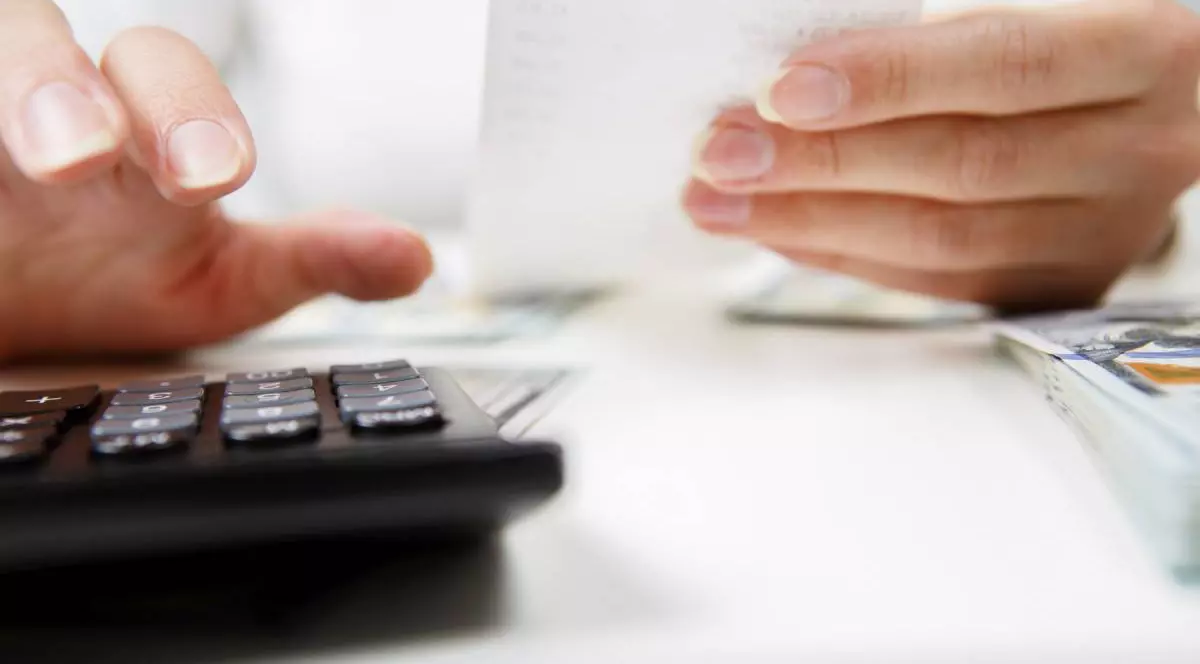 prim-plan cu mâini cu calculator care numără bani și își iau notițe acasă. Conceptul de economii