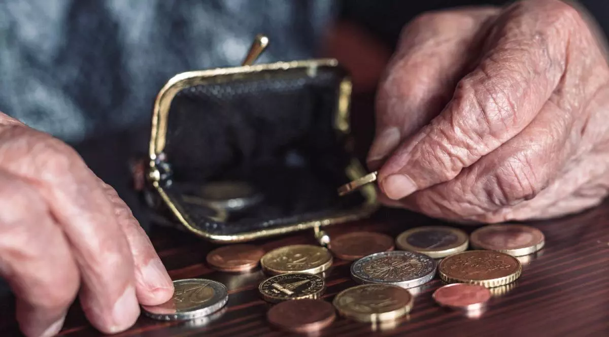 O femeie cu venituri extrem de mici, în timp ce își numără monedele de câte un euro dintr-un portofel. Banii primiți din ajutorul social sunt întinși pe o masă maro