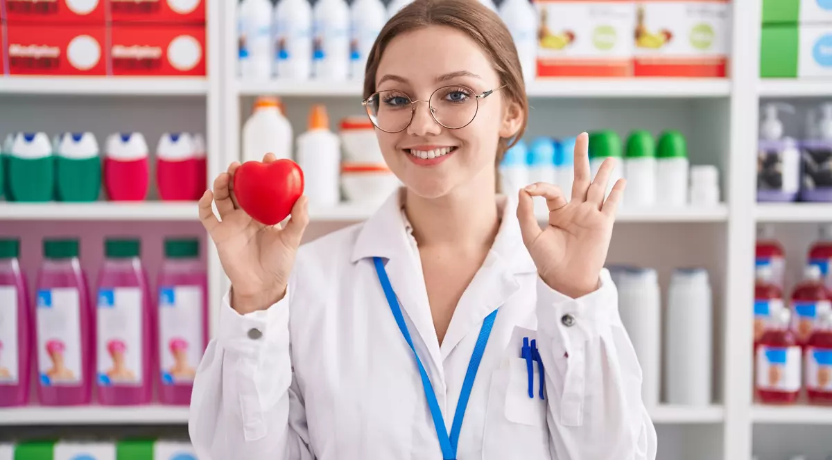 Farmacista, tine in mana dreapta o figurina rosie a unui inimi, iar cu cealalta mimeaza semnul ok