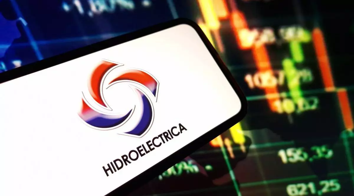 Un telefon pe ecranul căruia apare logo-ul de la Hidroelectrica, iar în spatele lui se vede ecranul unui laptop unde sunt publicate cifre referitoare la consumul din facturile de energie