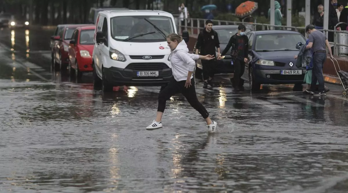 O femeie sare într-o baltă pe timp de ploaie, pe stradă.