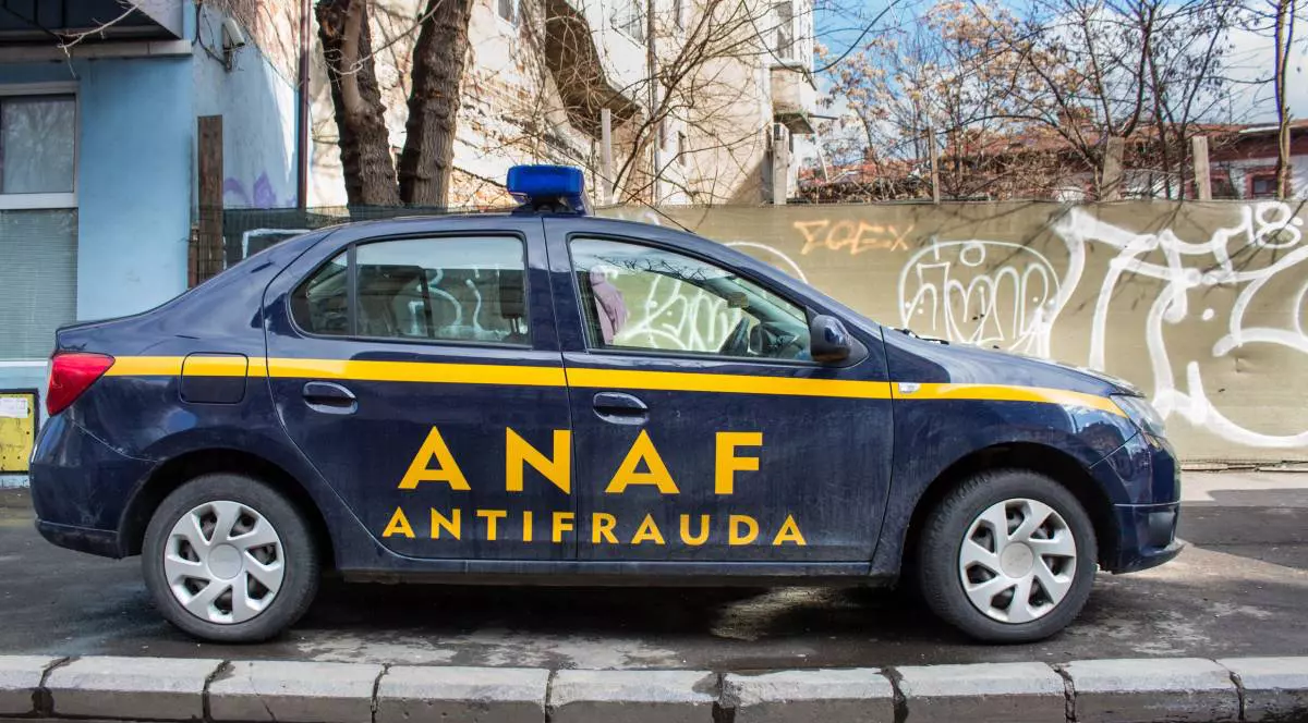 Masina albastru unchis a ANAF, Agentia Nationala Antifrauda, parcata pe o strada, in spate se vad copaci fara frunze, toamna