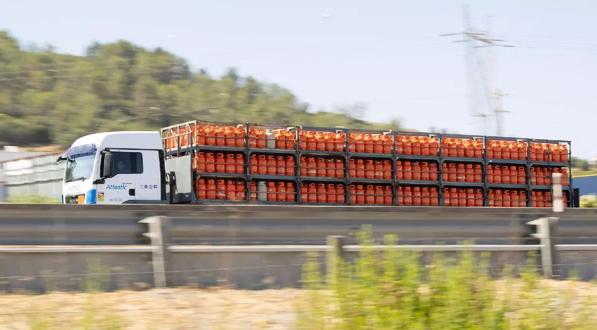 Camion alb transportând numeroase butelii de gaz portocalii pe autostradă