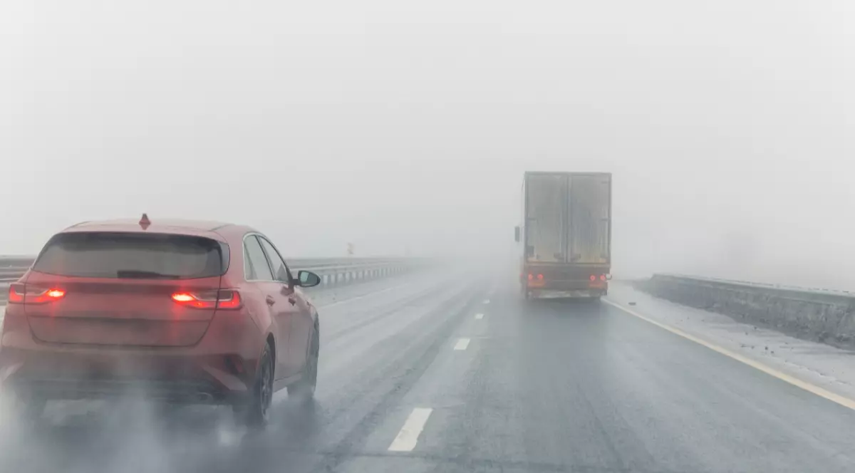 O mașină roșie și un TIR care circulă pe șosea, pe ceață