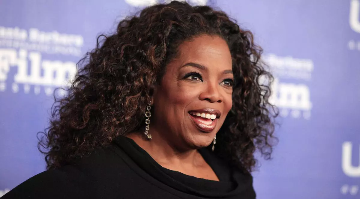 Oprah Winfrey, îmbrăcată cu o bluză neagră, pe fundal albastru