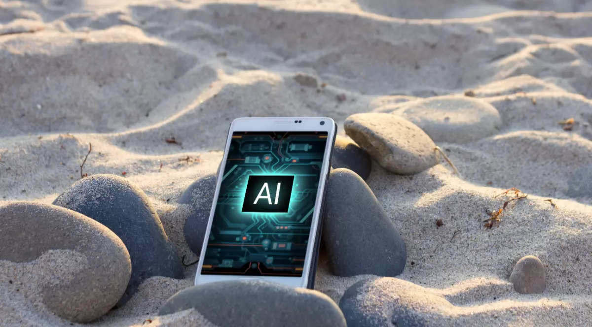 Un telefon pe care scrie cu litere mari AI. Acesta se află între pietre, pe nisip