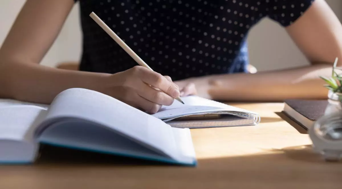 studentă care se pregătește pentru testul de facultate, examen, își ia notițe, face schițe, rezumatul manualului, studiază, citește o carte pentru raportul de curs. Prim-planul mesei de lucru pentru învățare