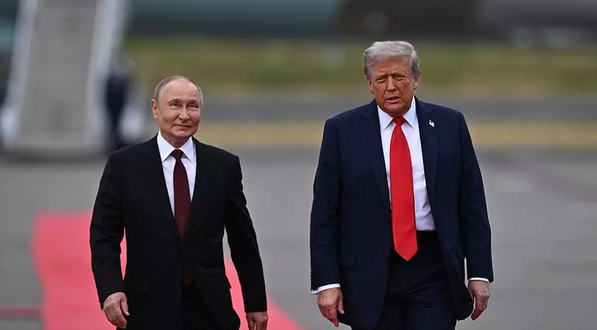 Imaginea îi prezintă pe Vladimir Putin și Donald Trump mergând unul lângă celălalt pe o pistă de aterizare sau o platformă, cu o porțiune de covor roșu sub picioarele lui Putin. Ambii bărbați sunt îmbrăcați în costume închise la culoare; Trump poartă o cravată roșie, în timp ce Putin poartă o cravată roșu închis sau burgund.