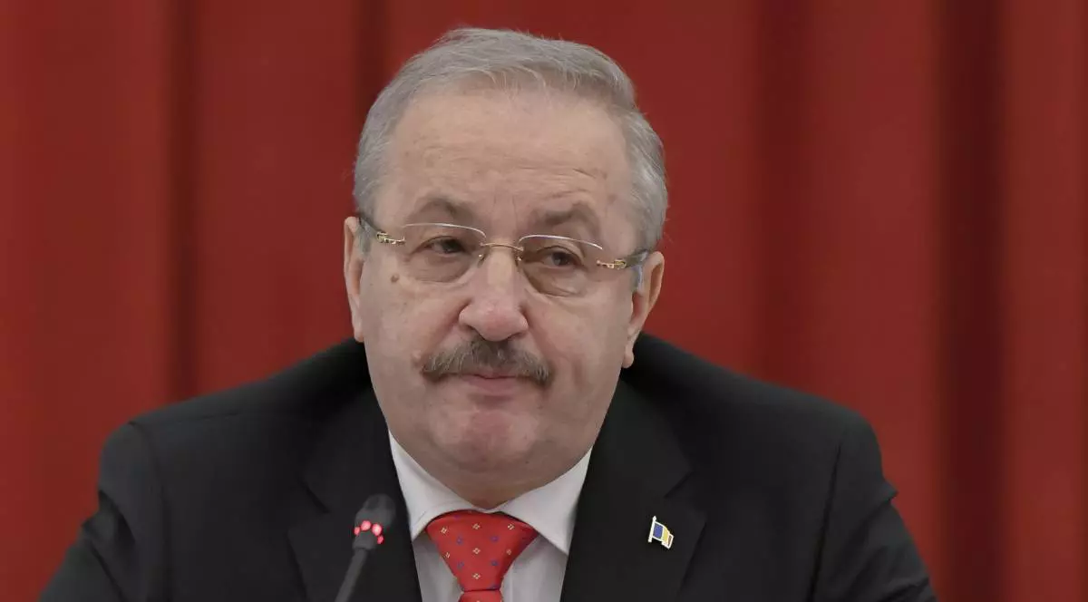 Vasile Dîncu, în timpul unei conferințe de presă la PSD, în spatele său este montată o draperie roție, social-democratul vorbește la microfon și poartă un costum negru cu o cravată roșie
