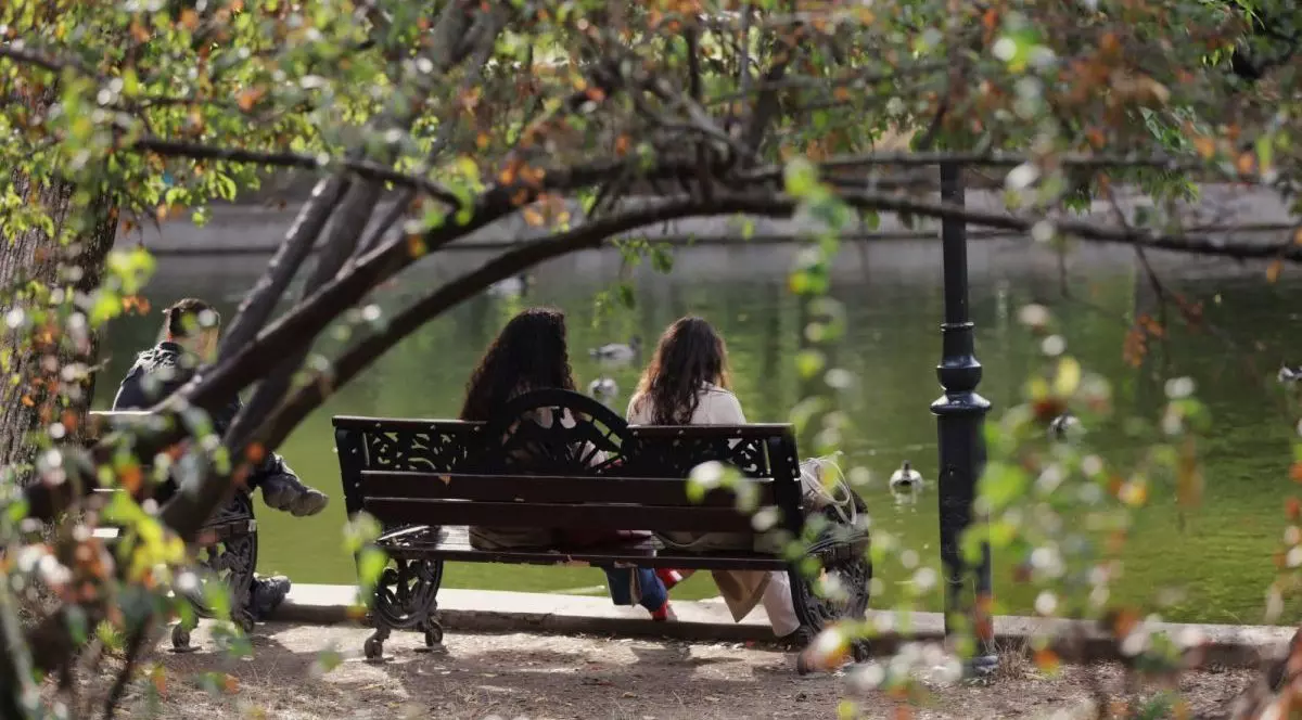 Două fete stau cu spatele pe o bancă, iar în fața lor este lacul Cișmigiu și se văd câteva rațe, într-o zi caldă de toamnă, octombrie 2025