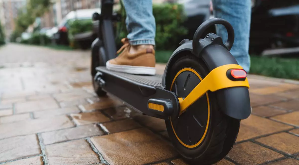 Un adolescent pe o trotinetă electrică, acesta are pantofi maro și blugi albaștrii