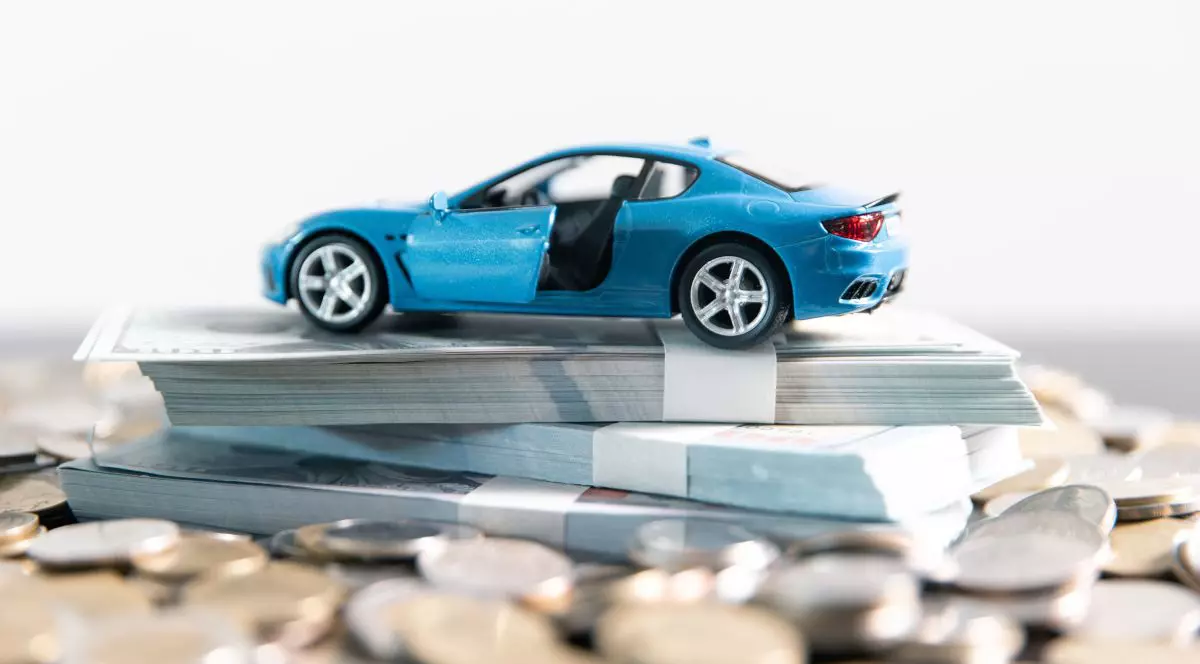 Mașinuță de jucărie, de culoare albastră, peste bancnote de bani, pe fundal alb