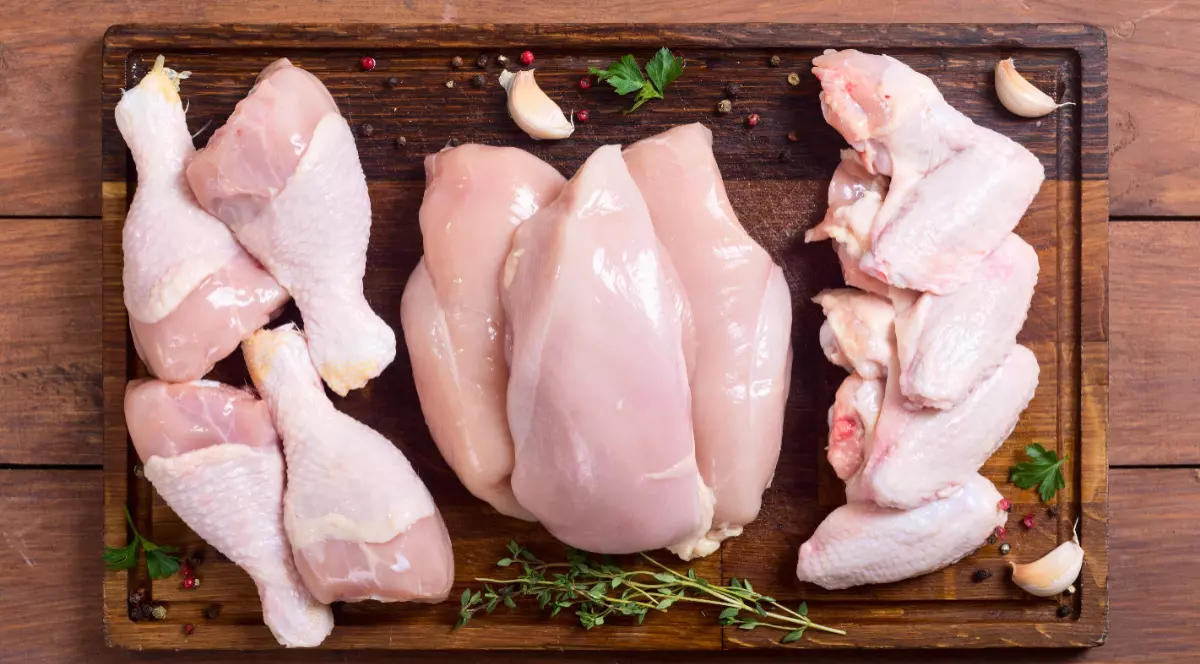 Pulpe, piept și aripioare de pui nepreparate pe un tocător.
