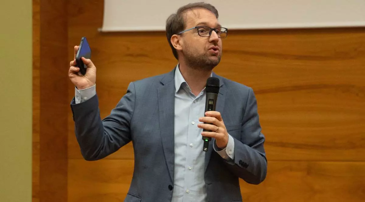 Primarul Timișoarei, Dominic Fritz, îmbrăcat la costum, în timpul unei conferințe la Primărie, vorbește la microfon într-o sală cu pereți maro