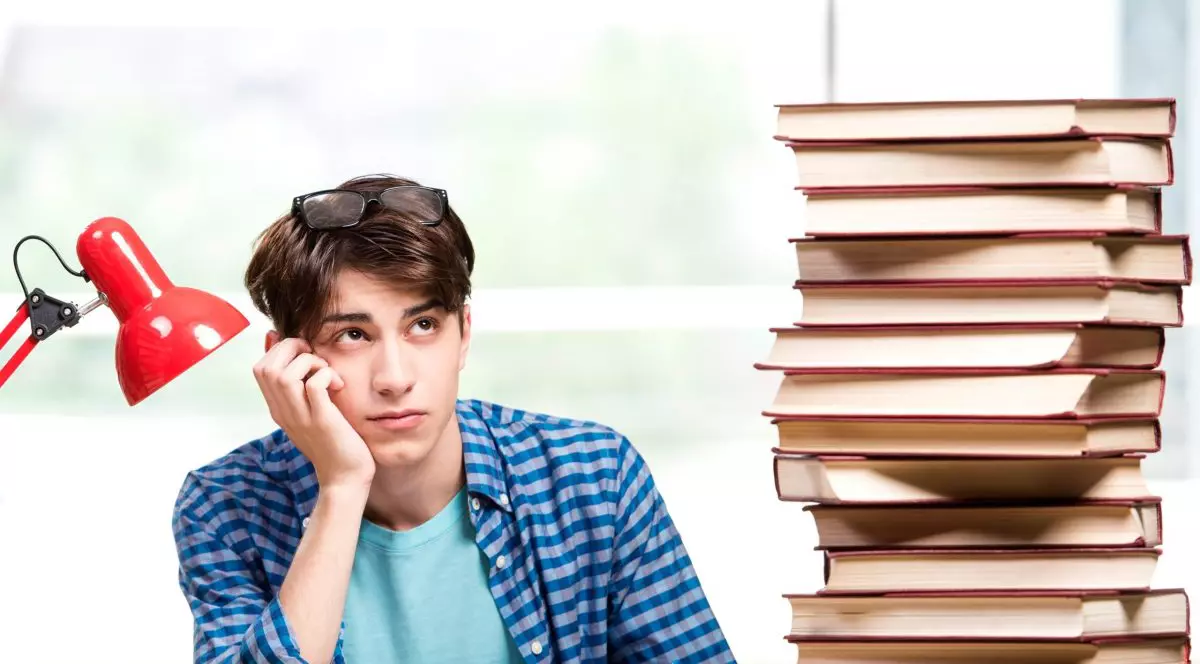 Elev care sta în bancă și are în față un teanc cu carți