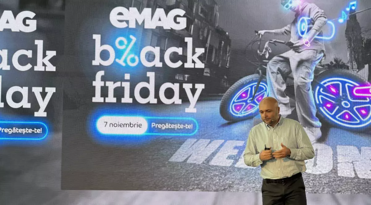 Bărbat îmbrăcat într-o cămașă verde prezintă evenimentul eMAG de Black Friday 2025, cu logo-ul campaniei afișat în spatele său pe un fundal digital.