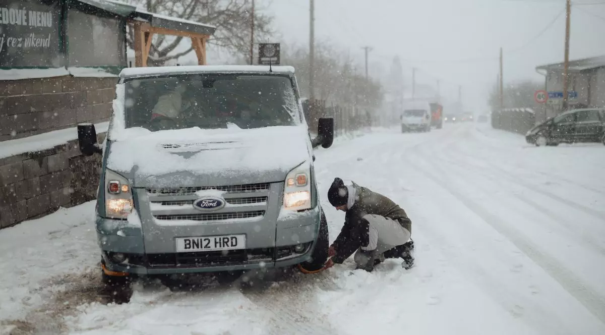 Un șofer își pune o centură de protecție împotriva zăpezii pe roțile din față ale dubei sale după ce drumul a fost acoperit de zăpadă, Slovacia, 30 martie 2023