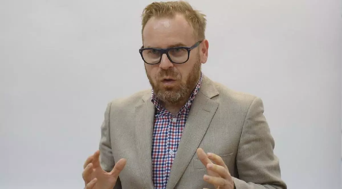 Judecătorul Mihail Udroiu, purtând ochelari, o cămașă în carouri roșii și albastre și un sacou gri deschis, vorbind și gesticulând