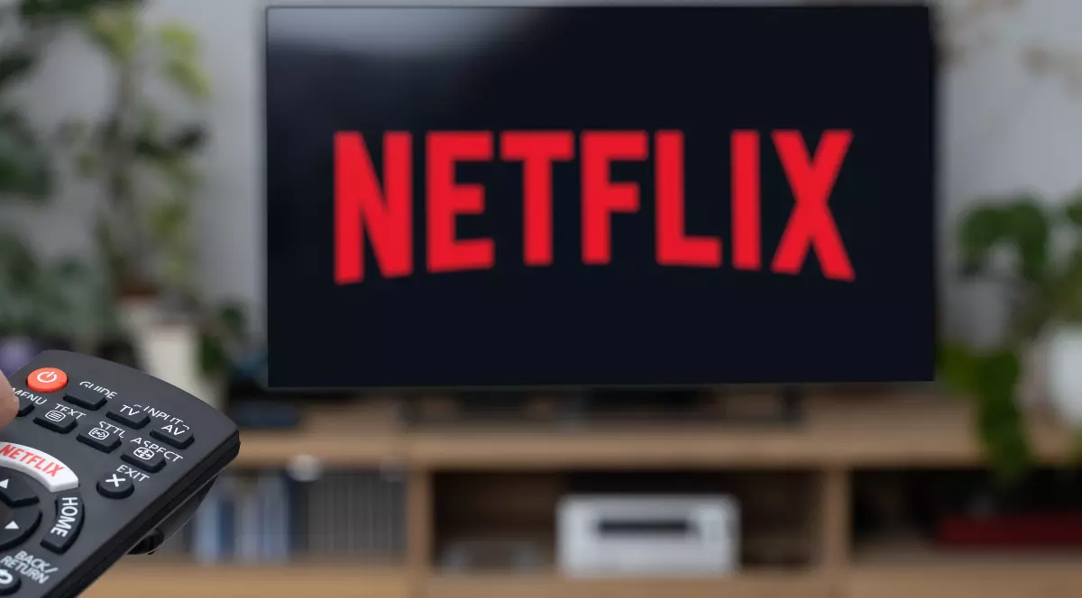 O persoană care ține o telecomandă în mână și deschide Netflix pe un televizor.